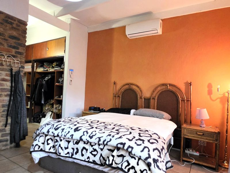 Bedroom featuring an exposed brick accent wall, built-in wardrobe storage, tiled flooring, and a wall-mounted air conditioning unit.