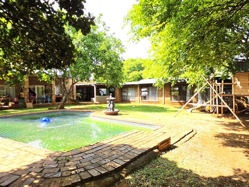 Spacious rear garden featuring a swimming pool with safety net, brick paving, mature trees, and direct access to the home via sliding doors.