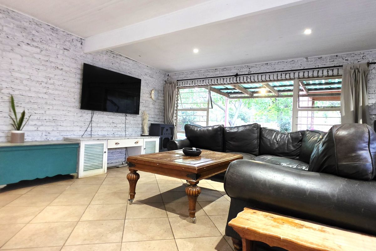 Spacious living room featuring an exposed brick feature wall, tiled flooring, and large windows providing natural light and access to the outdoor area.