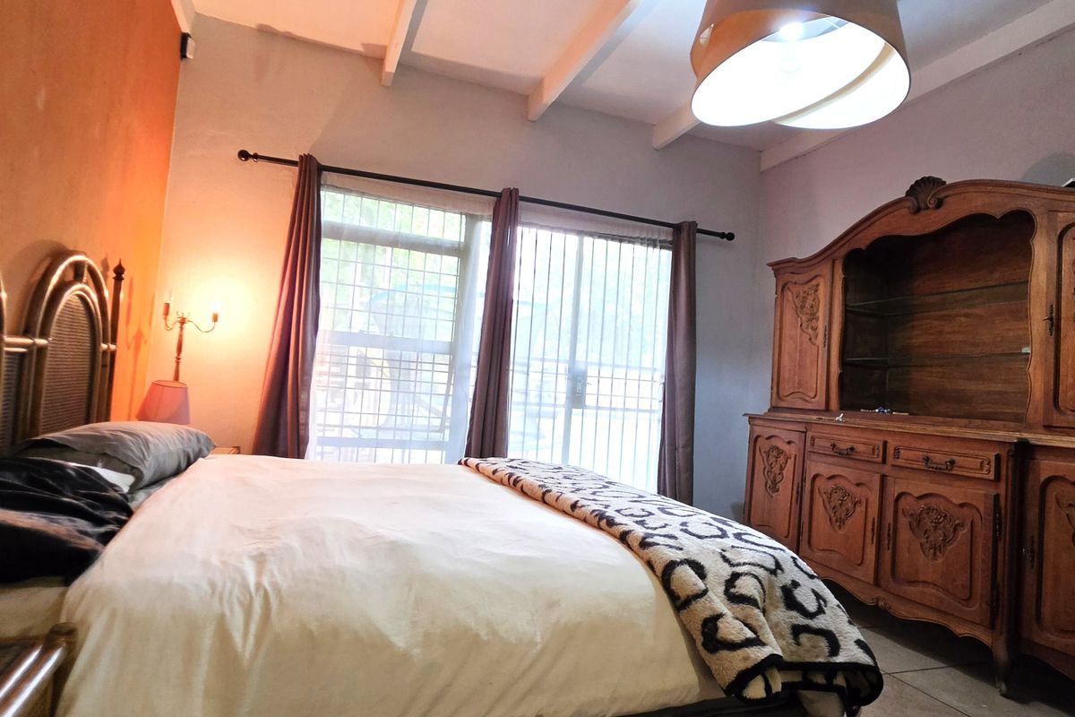 A bedroom featuring exposed ceiling beams, tiled flooring, and sliding glass doors with security bars, providing access to the exterior.