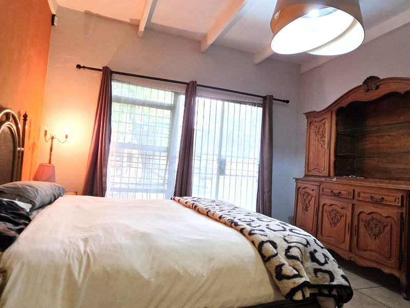 A bedroom featuring exposed ceiling beams, tiled flooring, and sliding glass doors with security bars, providing access to the exterior.