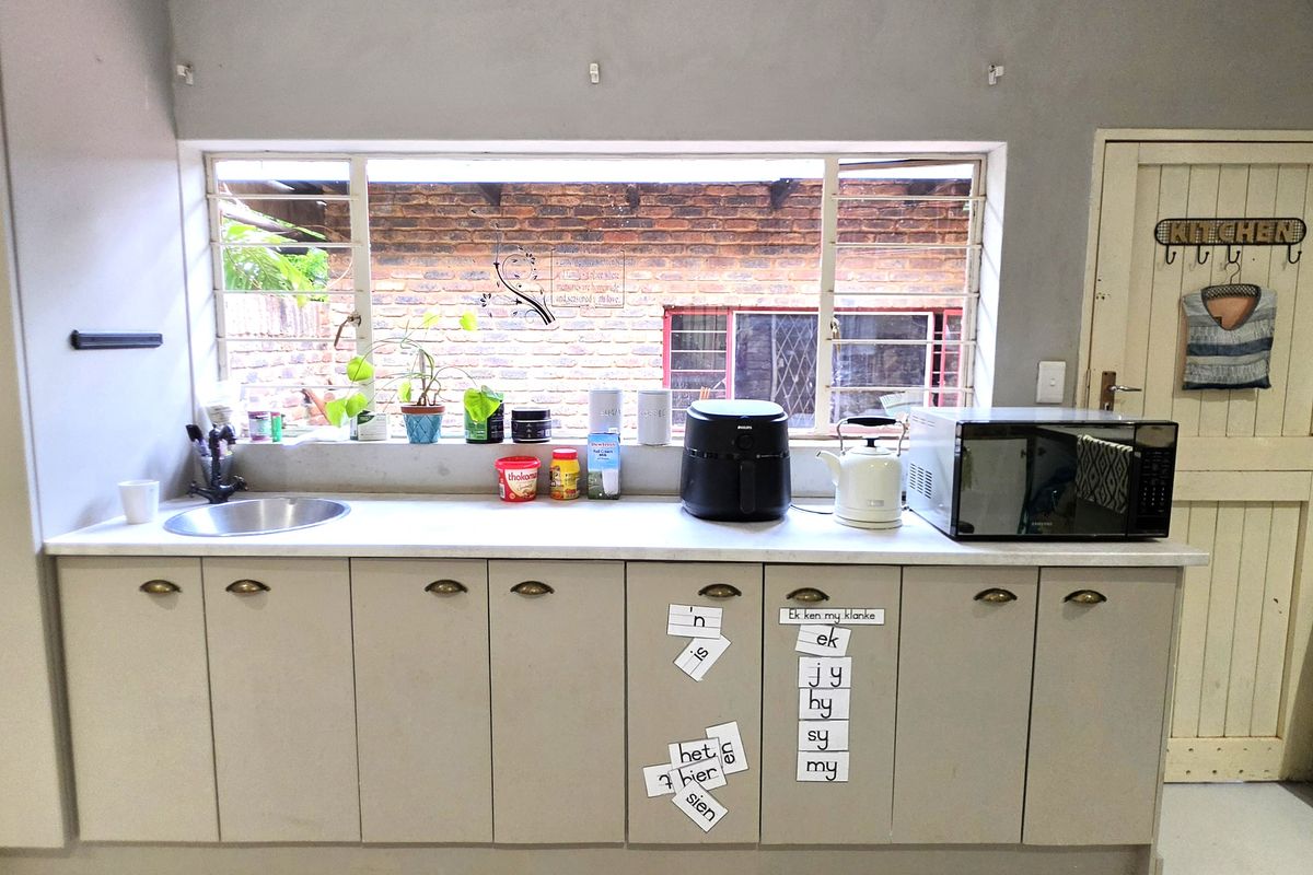 A functional kitchen area featuring built-in cabinetry, a stainless steel sink, and a window with security bars overlooking the exterior.