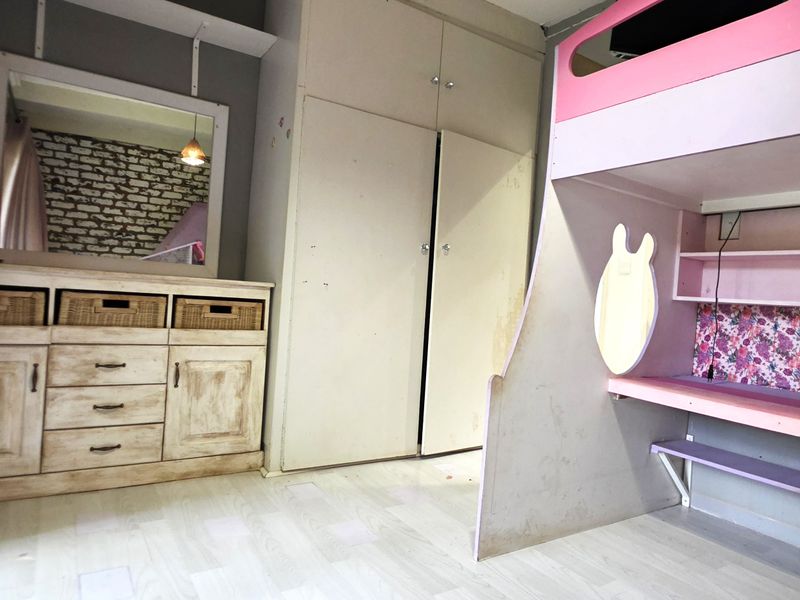 A bedroom featuring built-in cupboards, laminate flooring, and a large window, offering a functional space with potential for cosmetic updates.