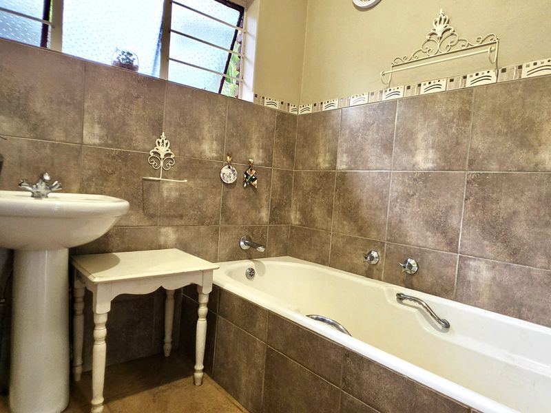 A functional bathroom featuring full-height wall tiling, a pedestal basin, and a built-in bathtub with chrome fixtures.