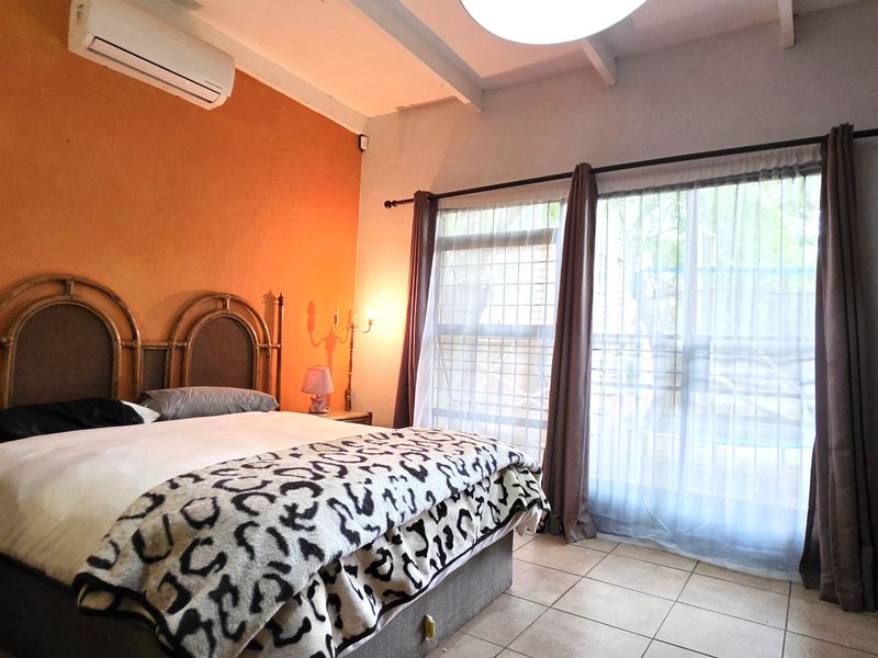 A bedroom featuring tiled flooring, exposed ceiling beams, and a wall-mounted split-system air conditioner, with large windows providing natural light.