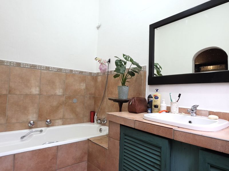 A functional bathroom featuring a built-in bathtub, tiled vanity countertop with a drop-in sink, and a wall-mounted mirror.