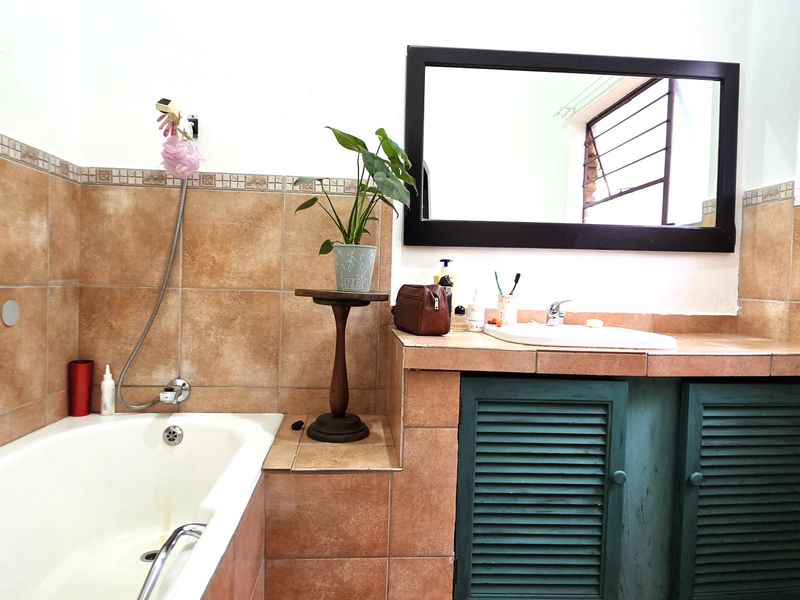 A functional bathroom featuring a built-in bathtub, tiled vanity with basin, and louvered storage cabinetry.