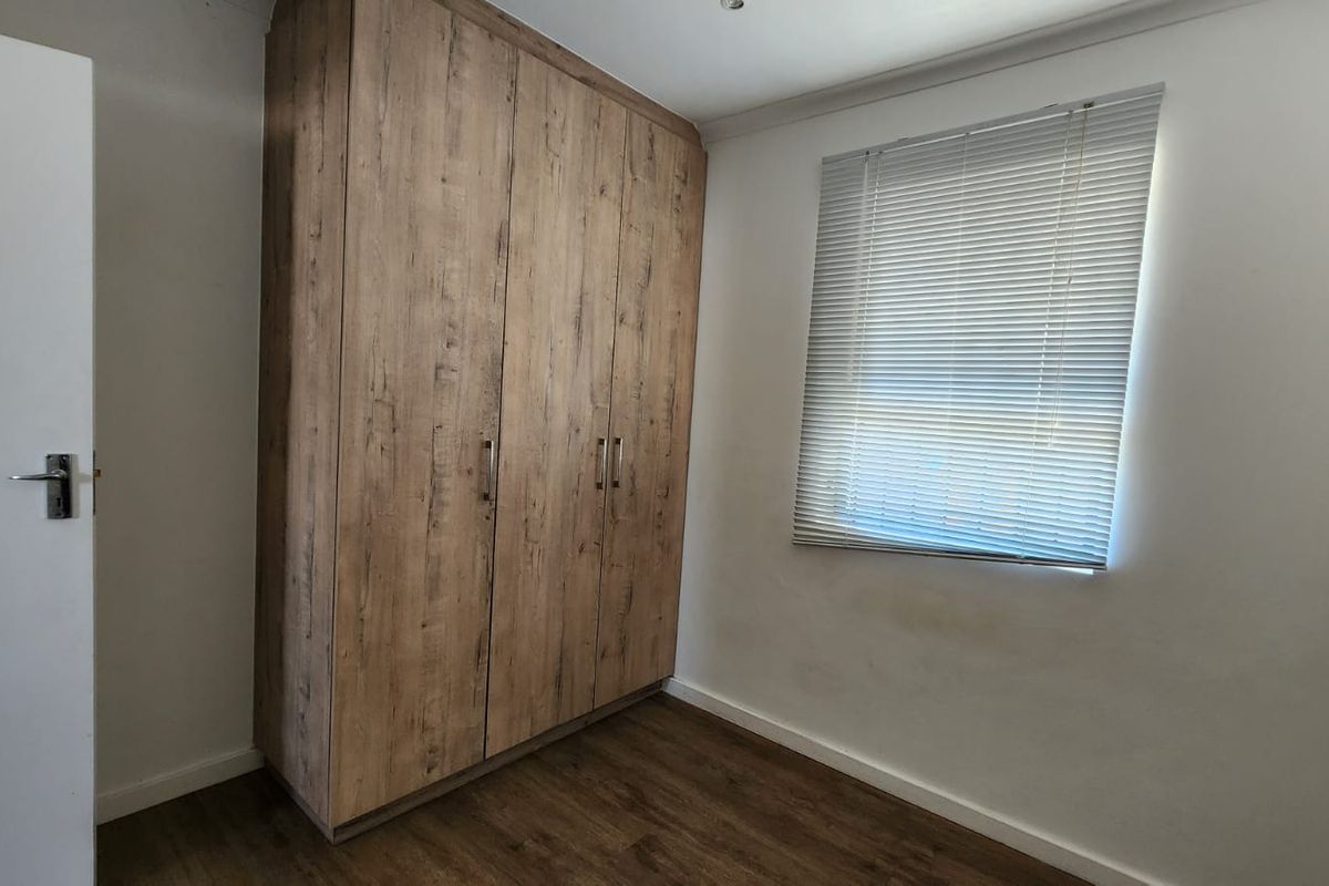 A clean, empty bedroom featuring wood-look laminate flooring, a large built-in wardrobe with a wood-grain finish, and window blinds.
