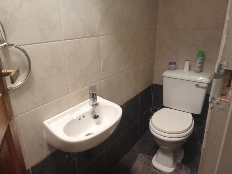 A compact guest bathroom featuring a wall-mounted basin, toilet, and two-tone tiled walls. The door frame shows visible signs of wear and damage.