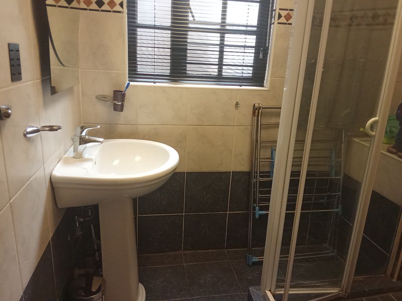 A functional bathroom featuring a pedestal basin, chrome mixer tap, shower enclosure, and tiled finishes throughout.