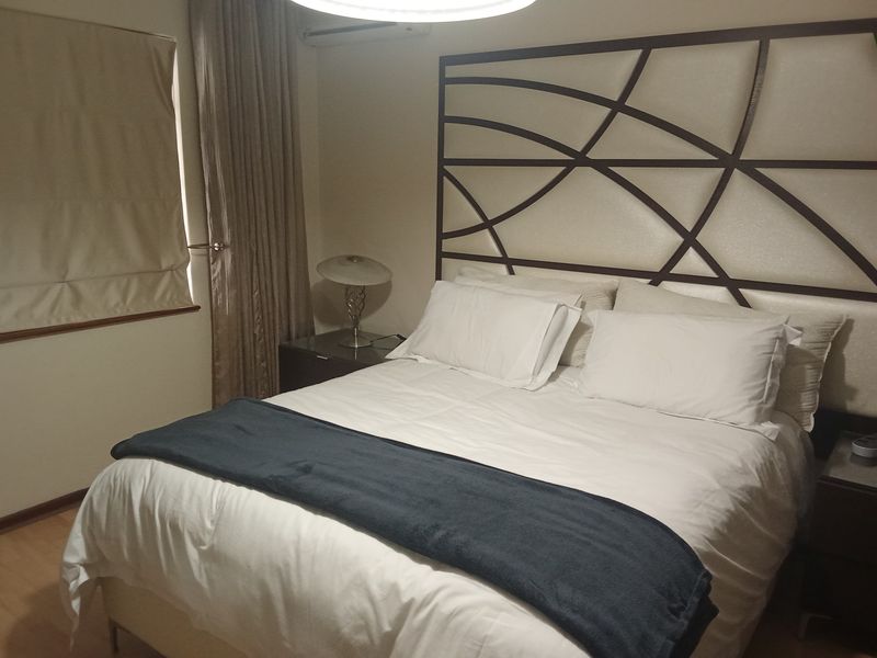 A well-maintained bedroom featuring laminate flooring, an integrated air conditioning unit, and neutral window treatments.