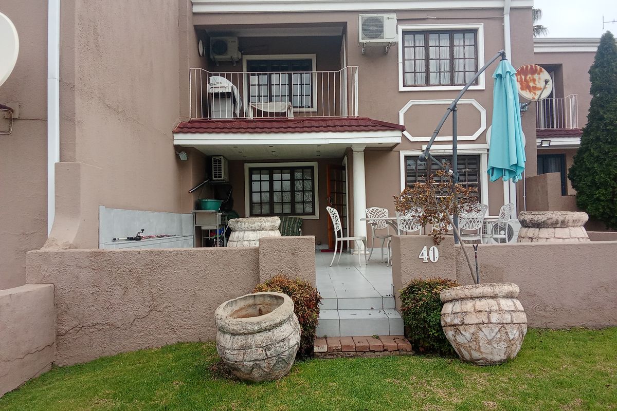 Rear view of the apartment featuring a ground floor patio, upper balcony, tiled flooring, and built-in exterior sink area.