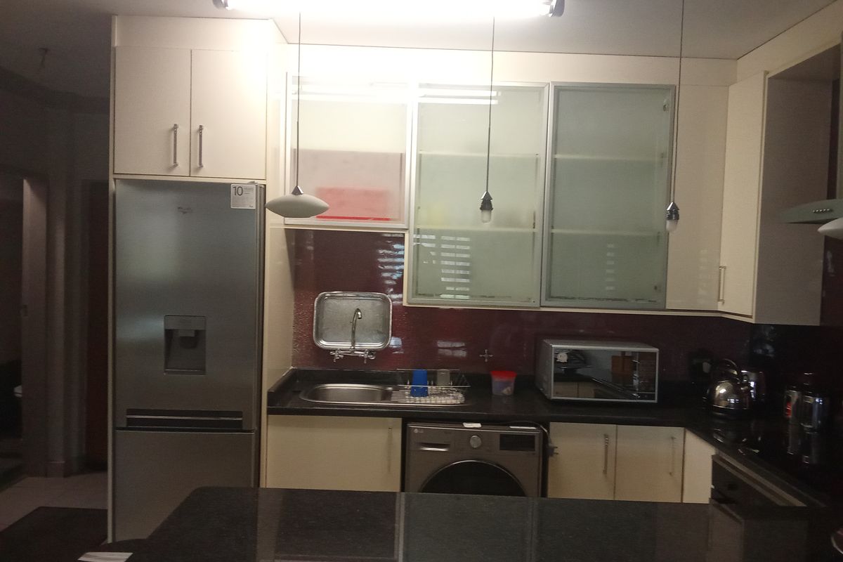 A functional kitchen featuring modern white cabinetry, dark granite countertops, a tiled backsplash, and integrated appliances including a washing machine.