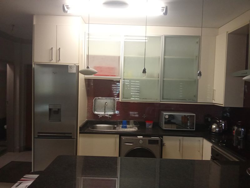 A functional kitchen featuring modern white cabinetry, dark granite countertops, a tiled backsplash, and integrated appliances including a washing machine.