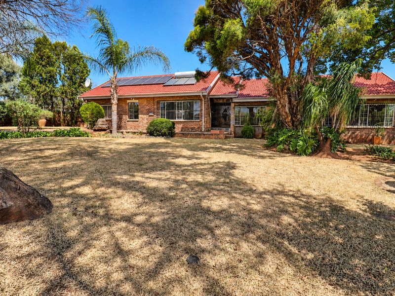 A rear view of a single-story brick house featuring a tiled roof, solar panels, and a spacious garden area with mature trees.