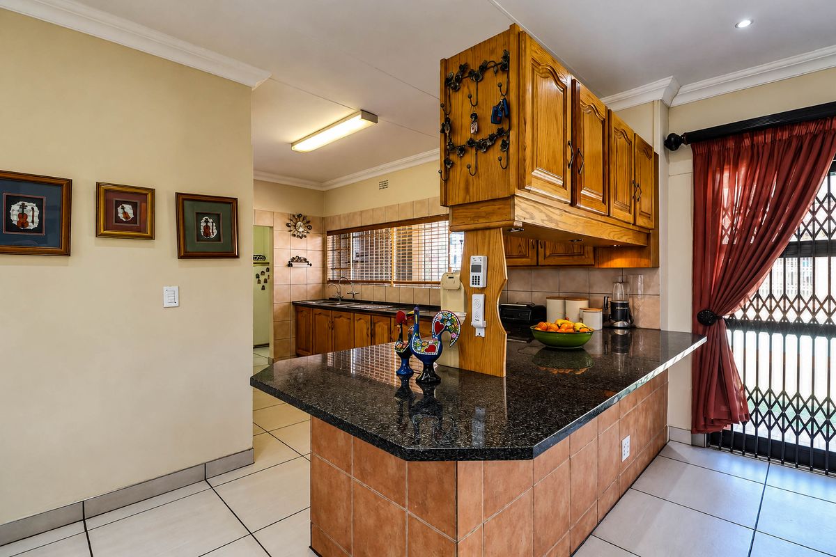 A functional kitchen featuring granite countertops, wooden cabinetry, and tiled flooring, with a breakfast bar area and direct access to an exterior security gate.