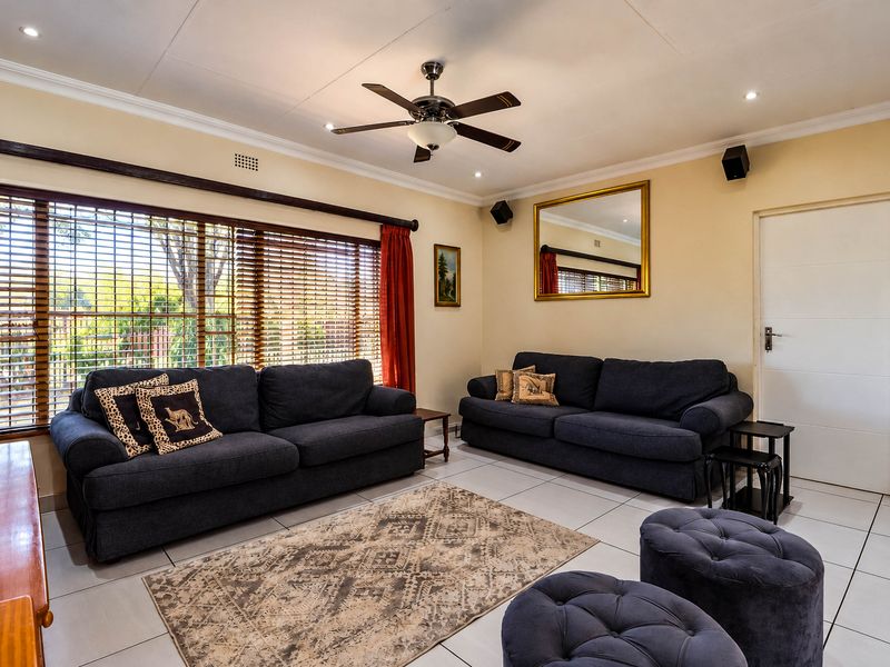 A well-maintained living room featuring tiled flooring, recessed lighting, a ceiling fan, and large windows with venetian blinds.