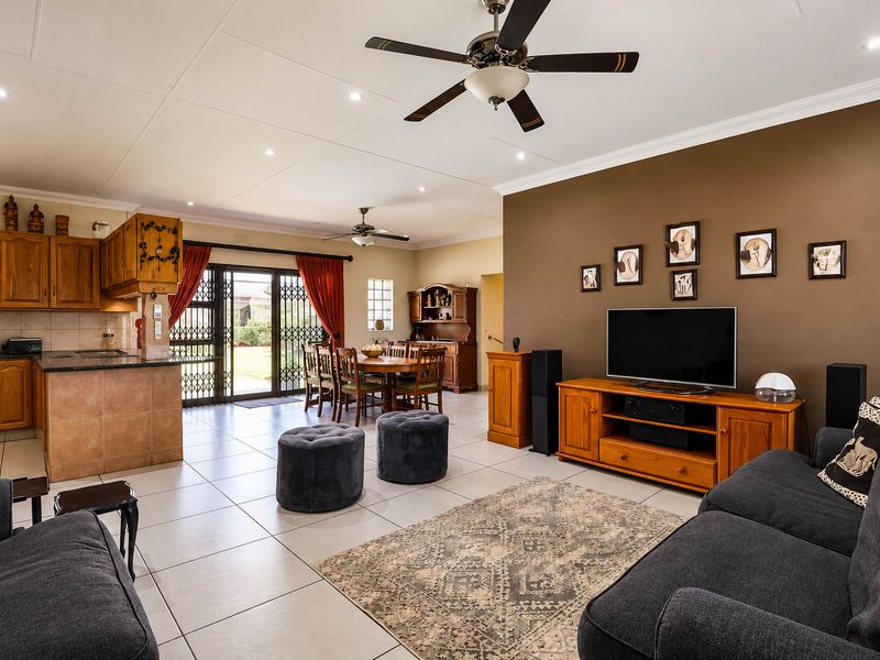 Spacious open-plan living and dining area featuring tiled floors, ceiling fans, and a functional kitchen with wooden cabinetry and direct garden access.