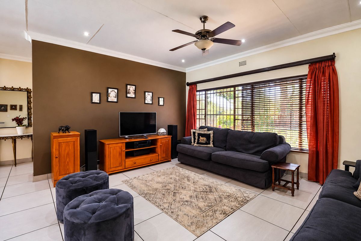 A well-maintained living room featuring tiled flooring, a ceiling fan, and large windows with venetian blinds, creating a comfortable and functional living space.