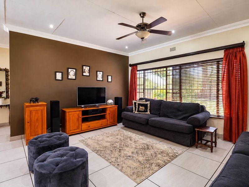 A well-maintained living room featuring tiled flooring, a ceiling fan, and large windows with venetian blinds, creating a comfortable and functional living space.
