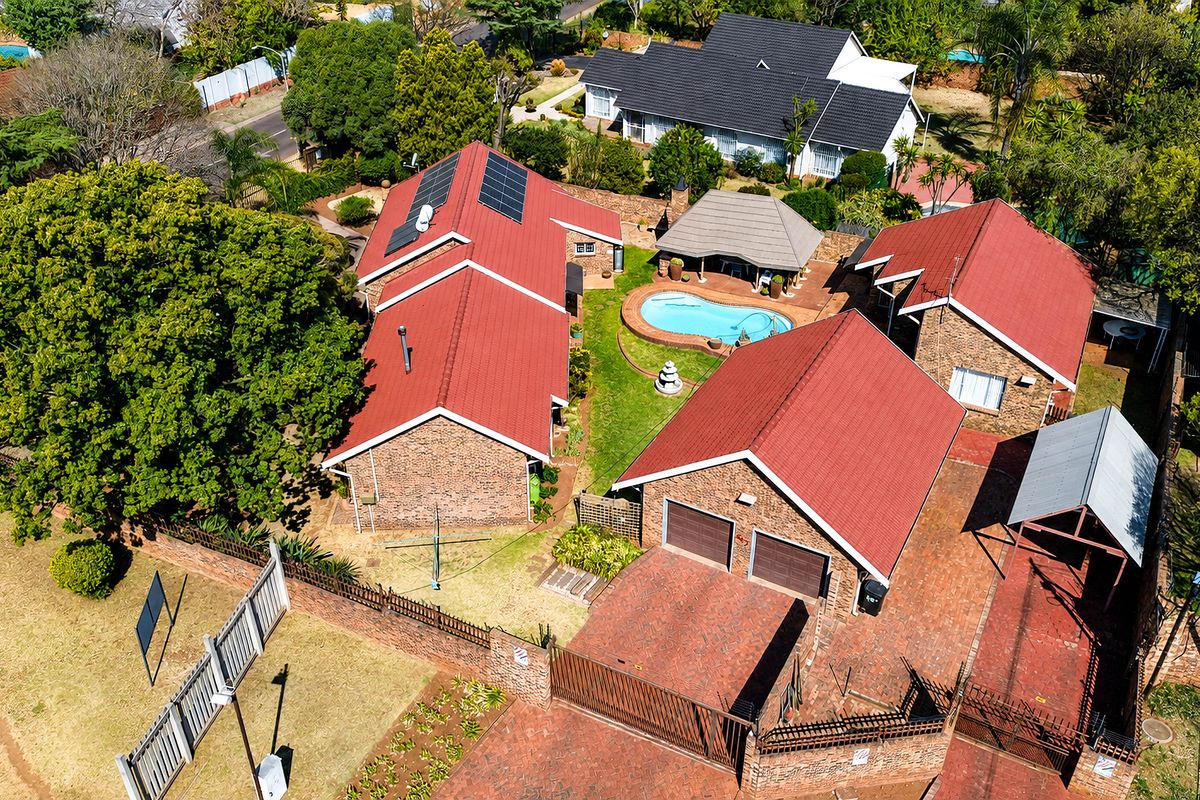 Aerial view of a residential property featuring multiple buildings with red metal roofs, a swimming pool, a lapa, and a double garage.