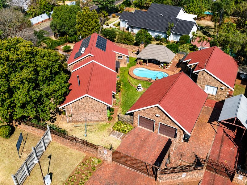 Aerial view of a residential property featuring multiple buildings with red metal roofs, a swimming pool, a lapa, and a double garage.