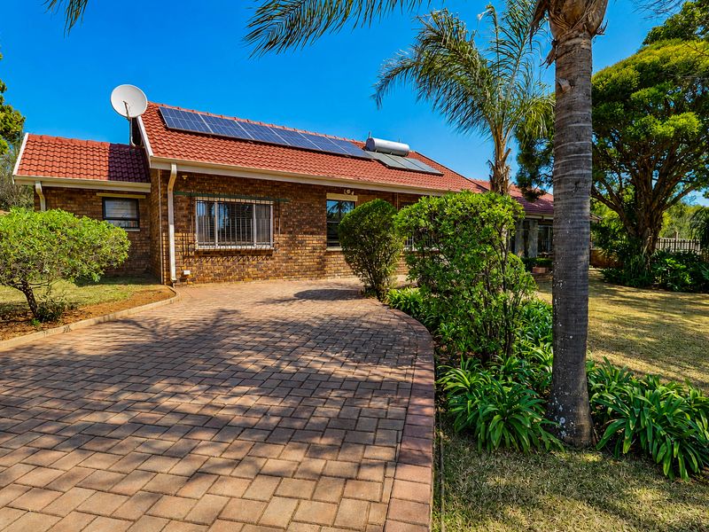 Front view of a brick house featuring a paved driveway, tiled roof with solar panels, and a solar water heating system.
