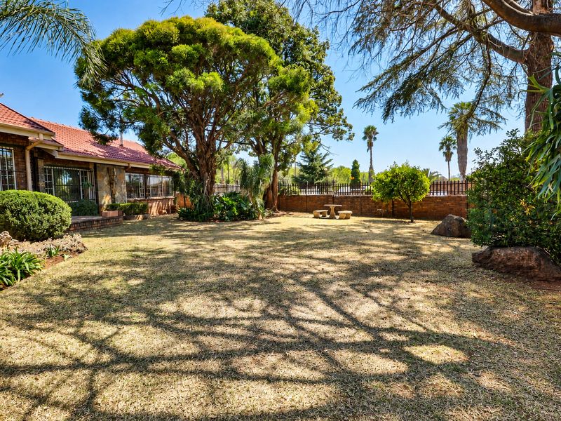 A spacious rear garden featuring mature trees, a brick boundary wall, and a view of the house with stone cladding and tiled roofing.
