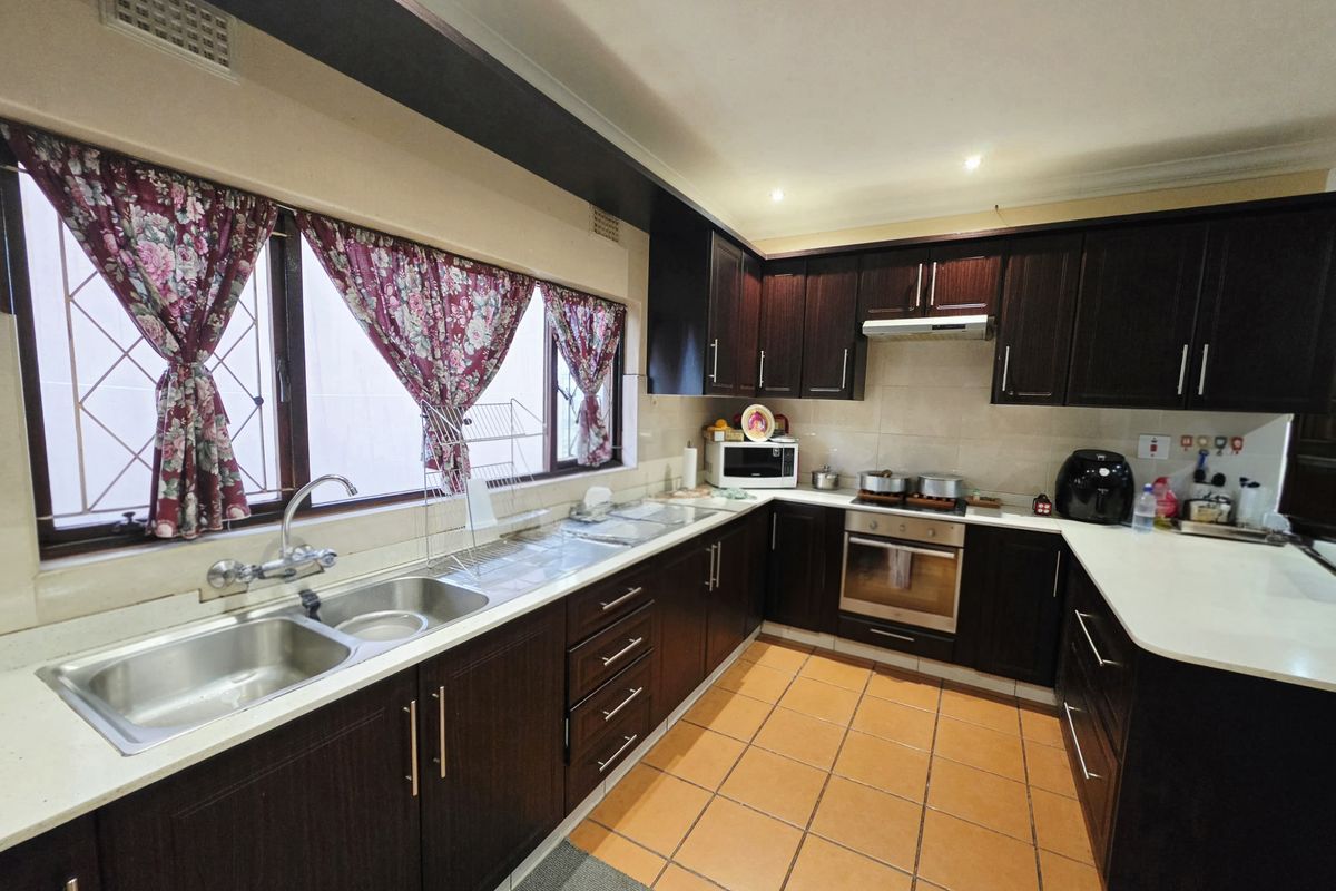 A functional kitchen featuring dark wood cabinetry, stone countertops, a double stainless steel sink, and built-in oven with extractor fan.