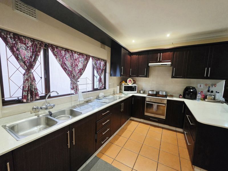 A functional kitchen featuring dark wood cabinetry, stone countertops, a double stainless steel sink, and built-in oven with extractor fan.