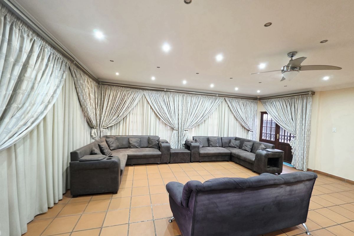 Spacious living room featuring terracotta floor tiles, recessed downlighting, and a ceiling fan, with extensive curtaining covering the walls.