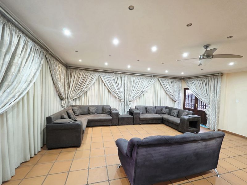 Spacious living room featuring terracotta floor tiles, recessed downlighting, and a ceiling fan, with extensive curtaining covering the walls.