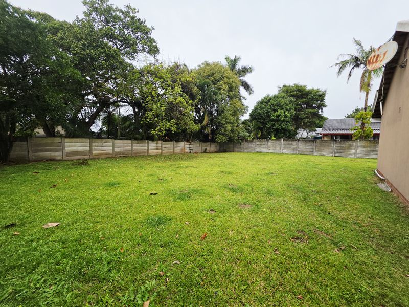 A spacious, level backyard featuring a well-maintained lawn enclosed by precast concrete boundary walls and mature perimeter trees.