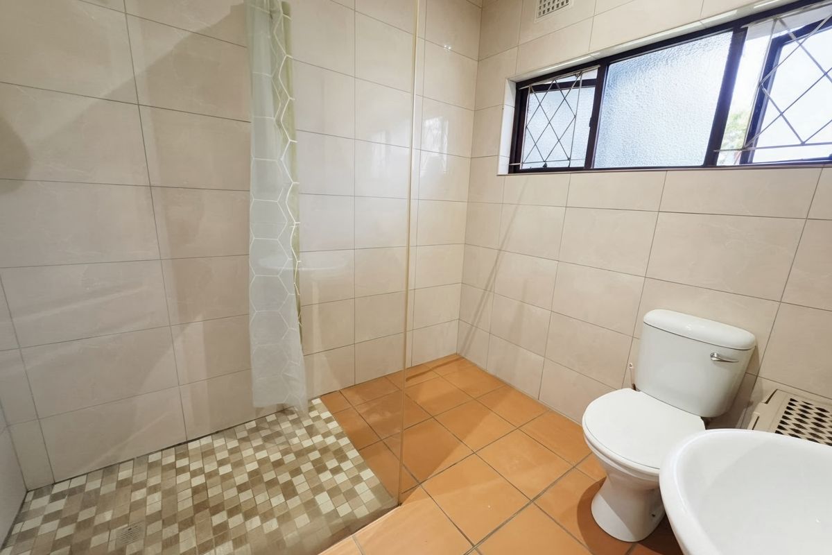 A functional bathroom featuring a walk-in shower with a glass screen, tiled walls and floors, a pedestal basin, and a toilet.