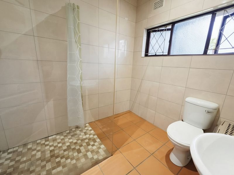 A functional bathroom featuring a walk-in shower with a glass screen, tiled walls and floors, a pedestal basin, and a toilet.