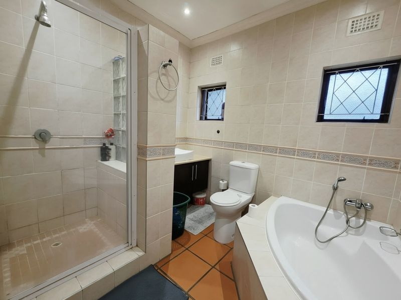 A functional bathroom featuring a separate shower enclosure, built-in bathtub, vanity unit, and toilet with neutral wall tiling.
