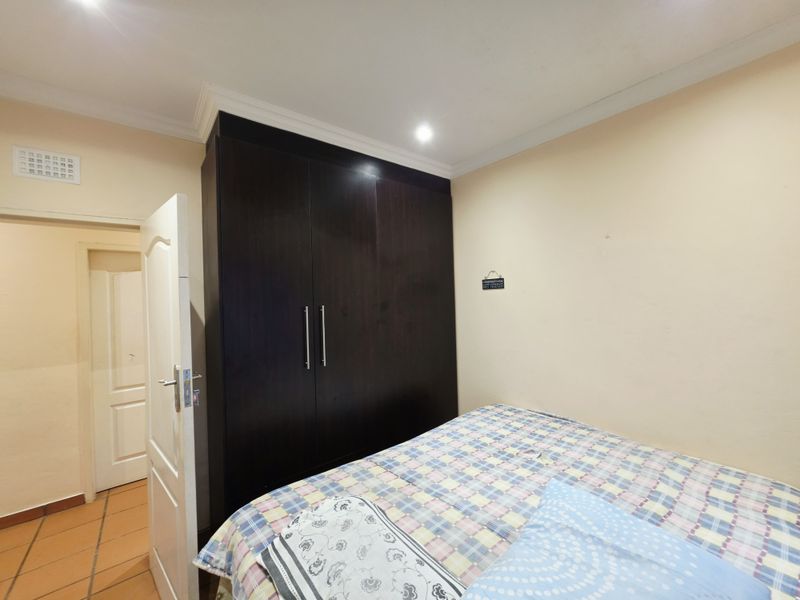 A bedroom featuring dark wood built-in cupboards, recessed ceiling lighting, and coved cornicing, providing functional storage and a neutral base.