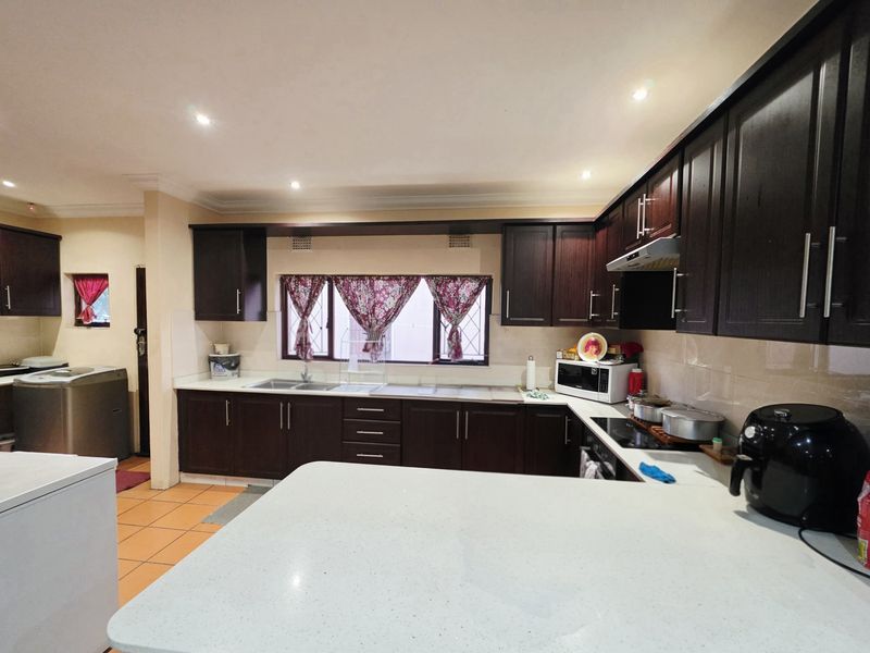 A functional kitchen featuring dark wood cabinetry, stone countertops, a double basin sink, and integrated lighting, offering ample storage and workspace.