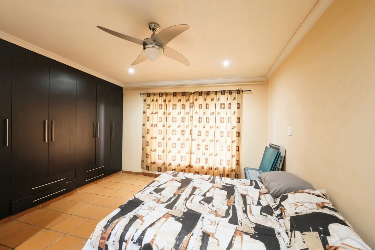 A bedroom featuring dark built-in cupboards, tiled flooring, and a ceiling fan, offering a functional space with neutral wall tones.