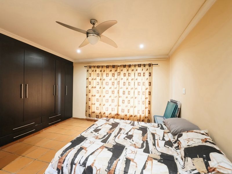 A bedroom featuring dark built-in cupboards, tiled flooring, and a ceiling fan, offering a functional space with neutral wall tones.