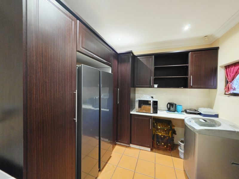 A functional scullery area featuring dark wood cabinetry, tiled flooring, and dedicated space for appliances.