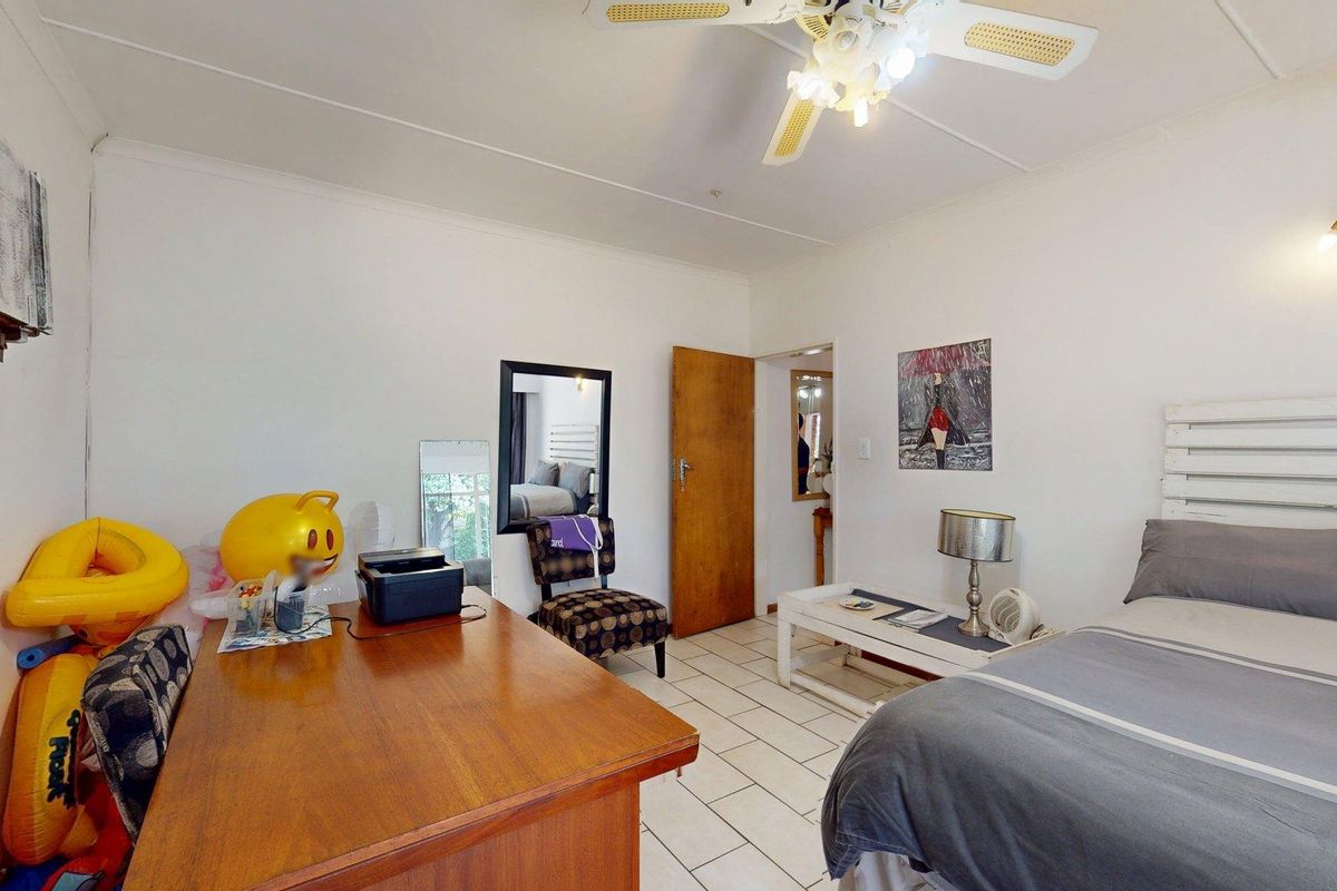 A functional bedroom featuring tiled flooring, a ceiling fan, and a wall-mounted light fixture, offering a neutral base for potential interior updates.