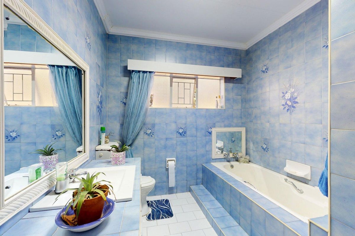 A dated bathroom featuring blue floral wall tiles, a built-in vanity with basin, and a tiled bathtub with integrated shower fixtures.