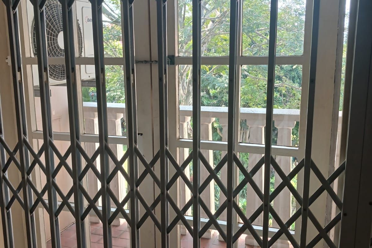 A view through a security gate onto a balcony featuring tiled flooring, a balustrade, and an external air conditioning unit.