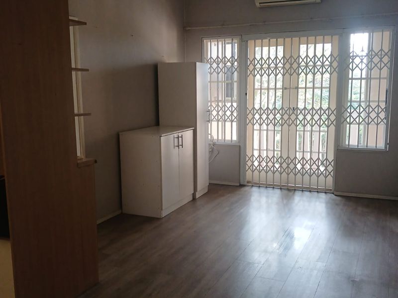 A spacious living area featuring laminate flooring, a wall-mounted air conditioner, and secure metal gates leading to the exterior.