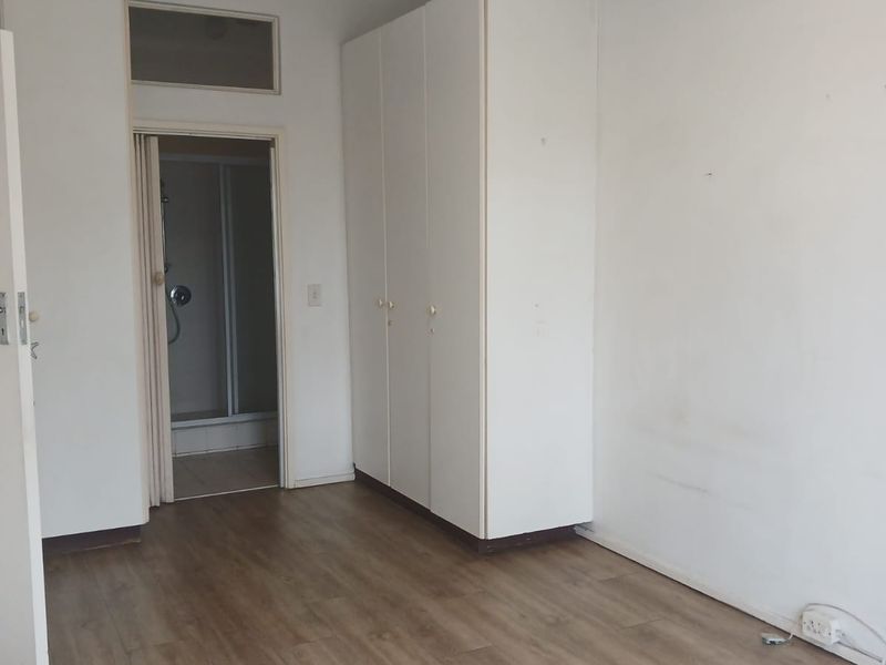 A vacant bedroom featuring laminate flooring, built-in cupboards, and direct access to an en-suite bathroom.