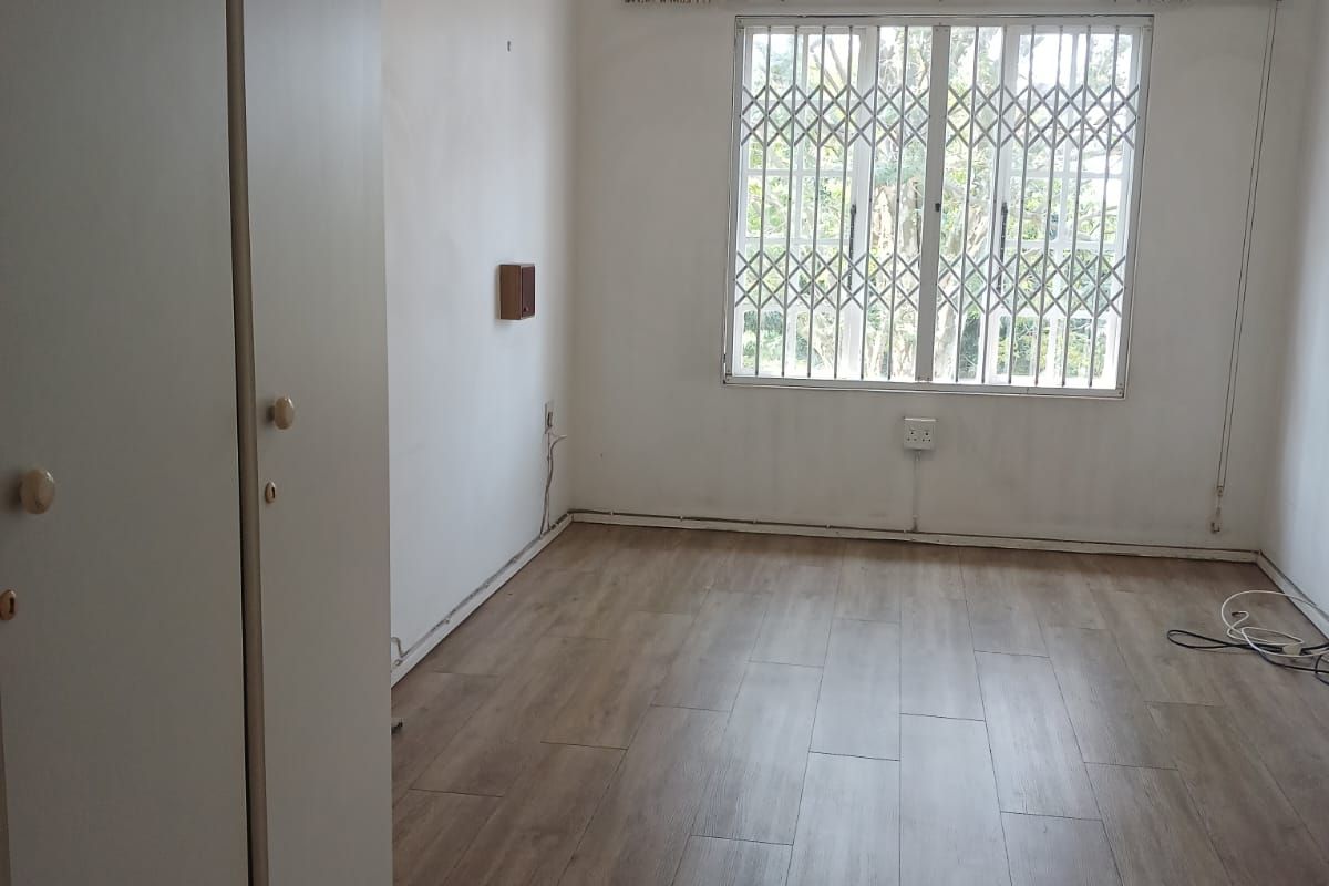 An empty bedroom featuring laminate flooring, built-in cupboards, a security gate on the window, and an installed air conditioning unit.