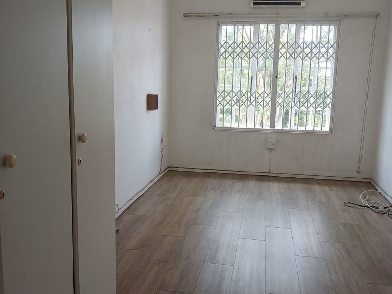 An empty bedroom featuring laminate flooring, built-in cupboards, a security gate on the window, and an installed air conditioning unit.