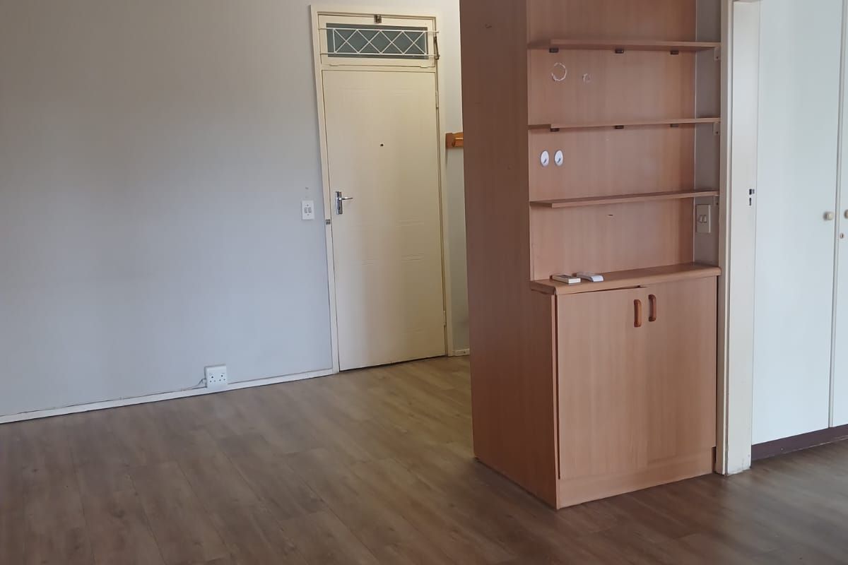 An empty living area featuring laminate flooring, a built-in wooden storage unit, and neutral wall finishes, providing a blank canvas for interior design.