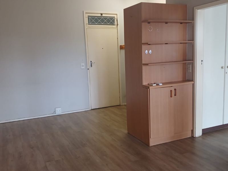 An empty living area featuring laminate flooring, a built-in wooden storage unit, and neutral wall finishes, providing a blank canvas for interior design.